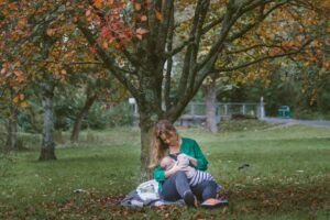 Uma mãe amamentando seu bebê embaixo de uma árvore para representar a preocupação da cafeína e amamentação.