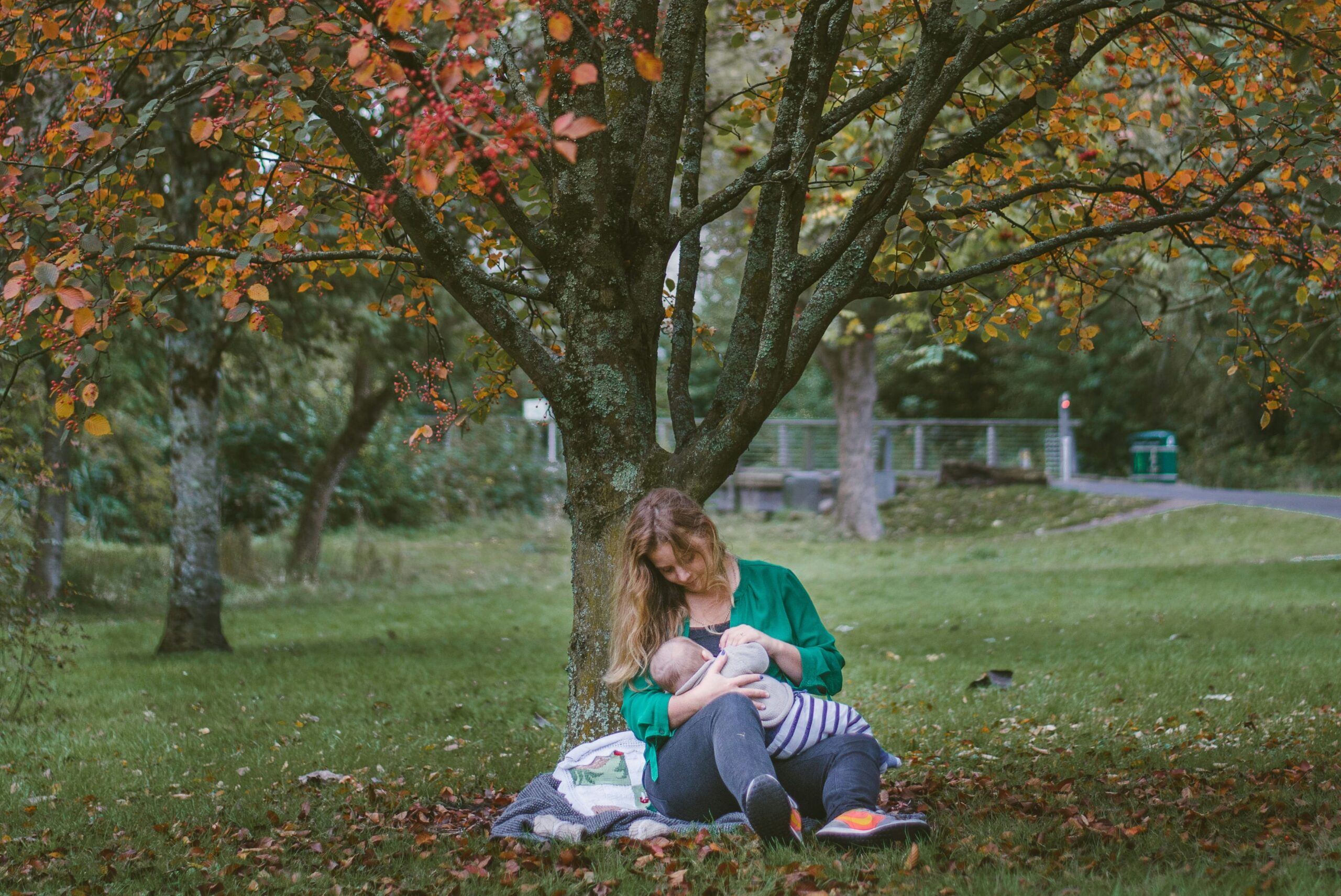 Uma mãe amamentando seu bebê embaixo de uma árvore para representar a preocupação da cafeína e amamentação.