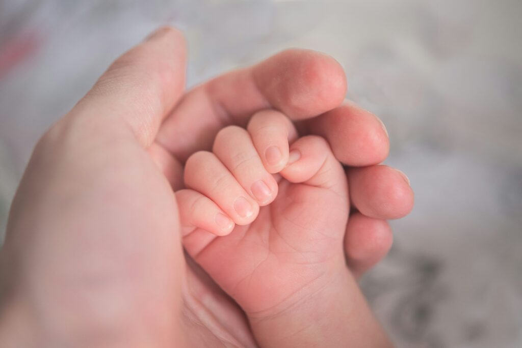 Mão de uma mãe segurando a mão do seu bebê, representando o rastreamento do desenvolvimento infantil
