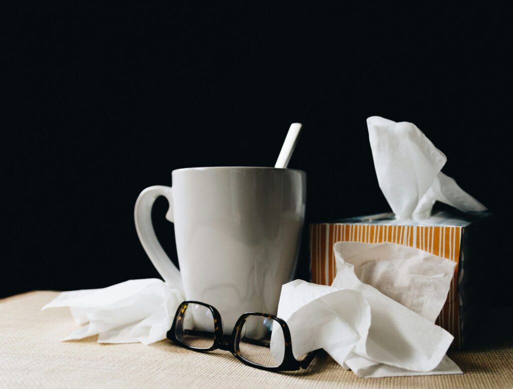 Uma mesa com uma caixa de lenços de papel e uma xícara com uma bebida quente, objetos que normalmente são usados por pessoas com resfriado comum.