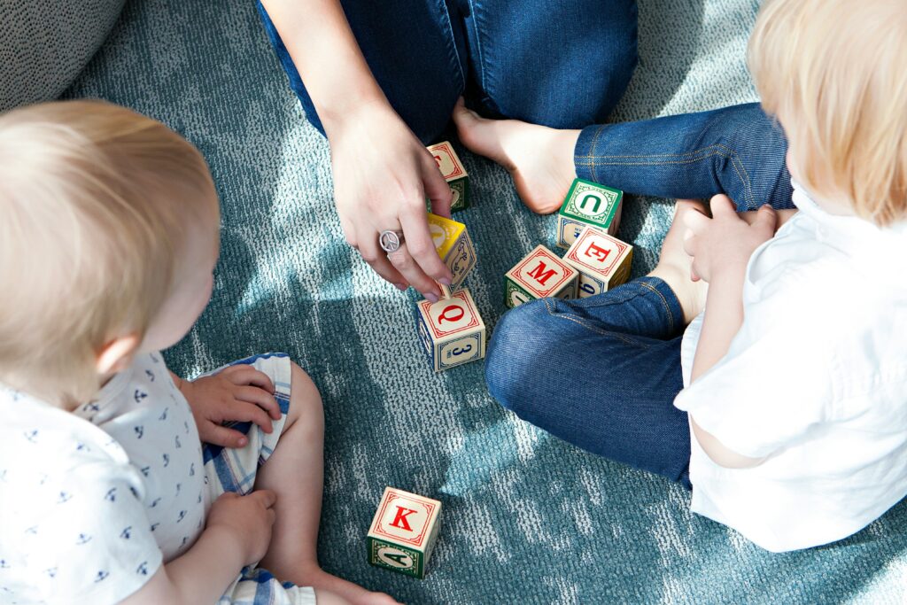 Crianças brincando com cubos contendo letras do alfabeto, representando atividades do desenvolvimento infantil