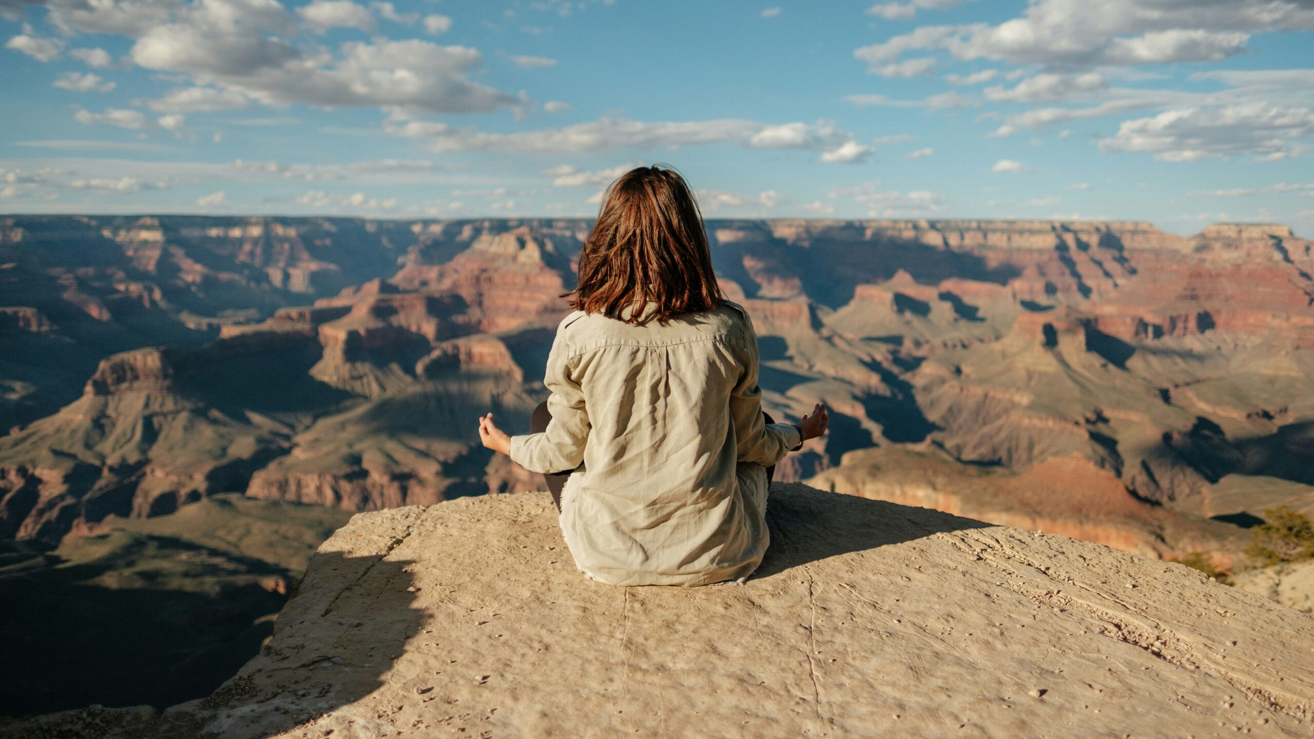 Imagem de uma mulher praticando meditação ao ar livre com a paisagem de montanhas ao fundo. Foto de Matteo Di Iorio na Unsplash