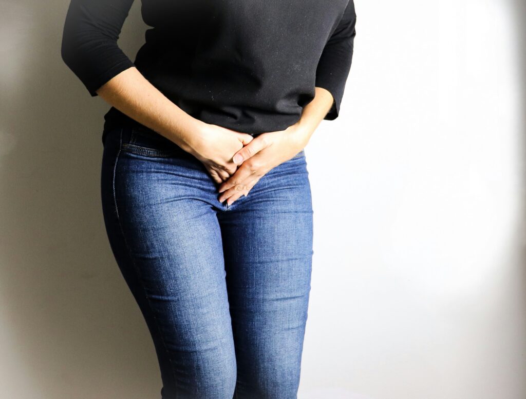 Imagem de uma mulher vestida com calça jeans e camiseta, com as mãos sobrepostas sobre suas partes íntimas, representando a suspeita de candidíase. Foto de Mayra Camargo na Unsplash
