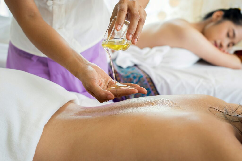Imagem de uma massagista colocando óleo nas mãos para fazer uma massagem na mulher que está deitada na mesa. Foto de alan caishan na Unsplash